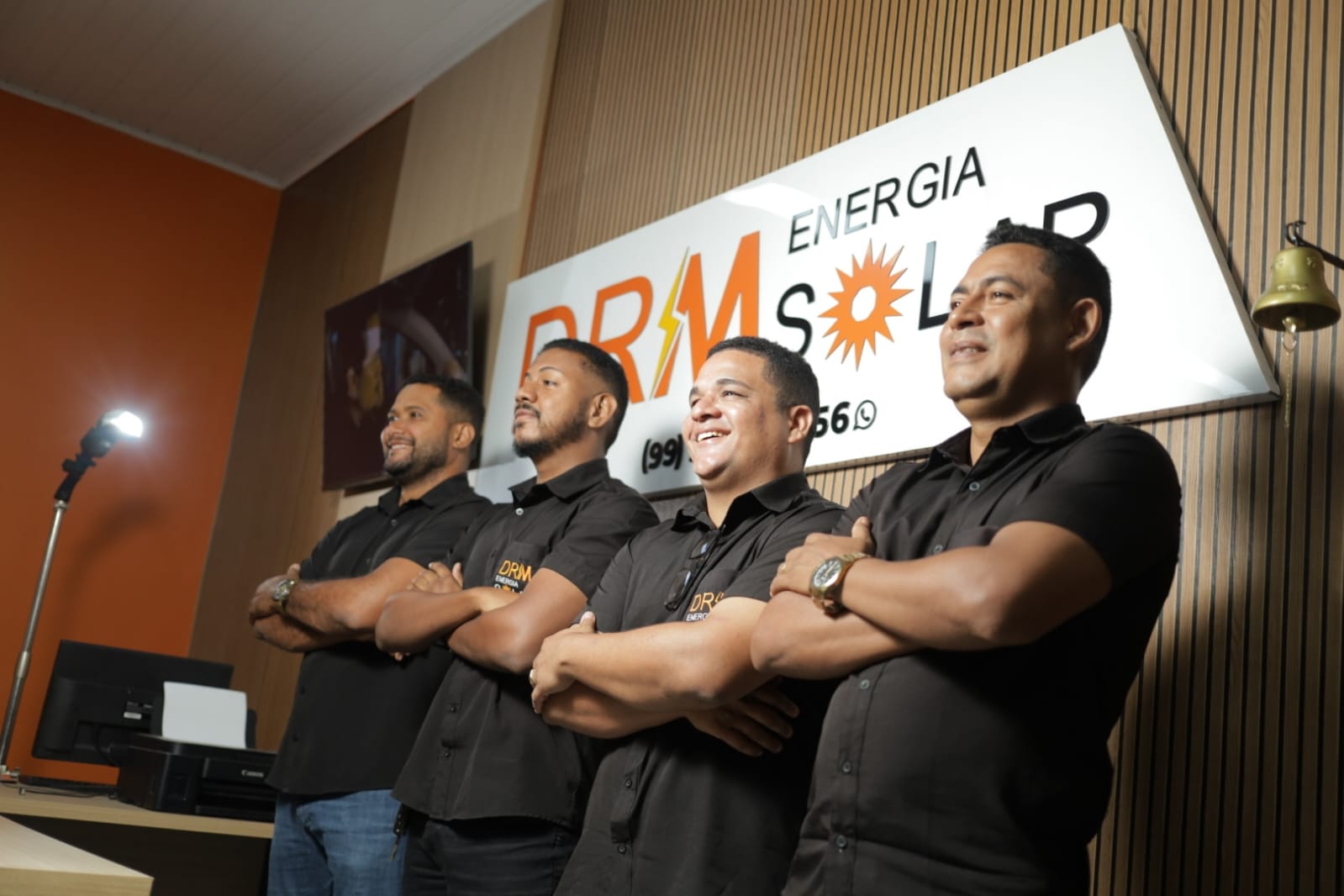 Quatro integrantes uniformizados da equipe DRM diante da marca da empresa