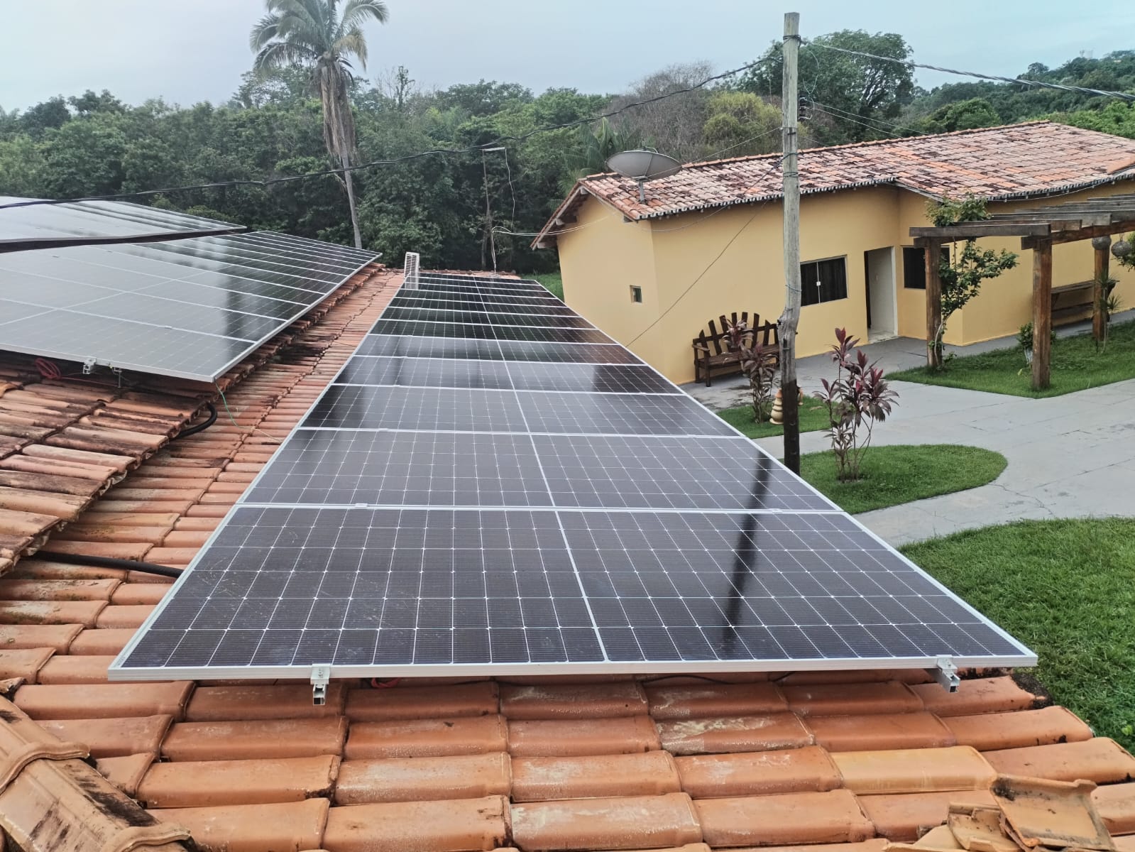 Instalação DRM em Itaguatins, Tocantins: painéis solares sobre telhado cerâmico, ao lado de uma casa amarela e jardim
